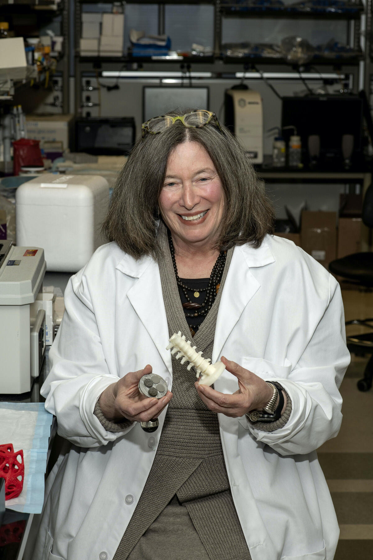 A woman wearing a lab coat and smiling while holding models of bones.