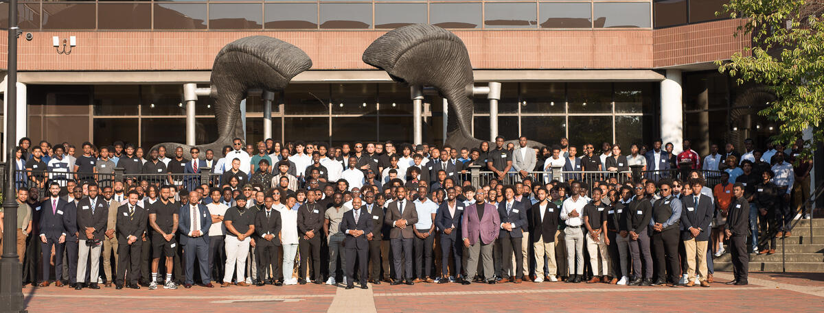 A large group of men standing in front of a ram horns statue 