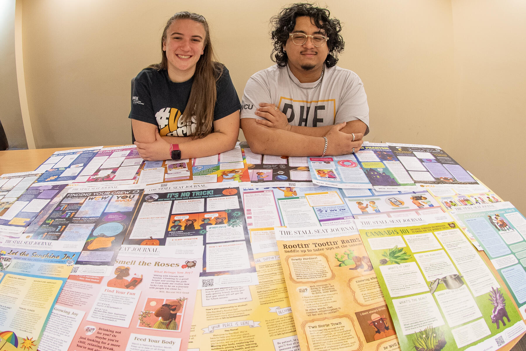 A photo of a woman and a man sitting at a table covered in flyers. 