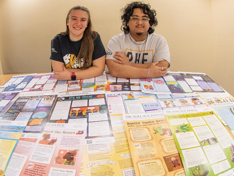 A photo of a woman and a man sitting at a table covered in flyers. 