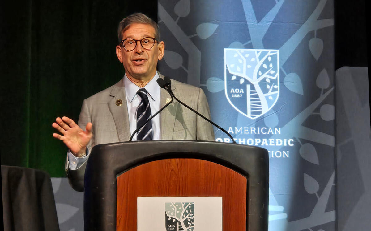 A photo of a man standing behind a podium and speaking. 