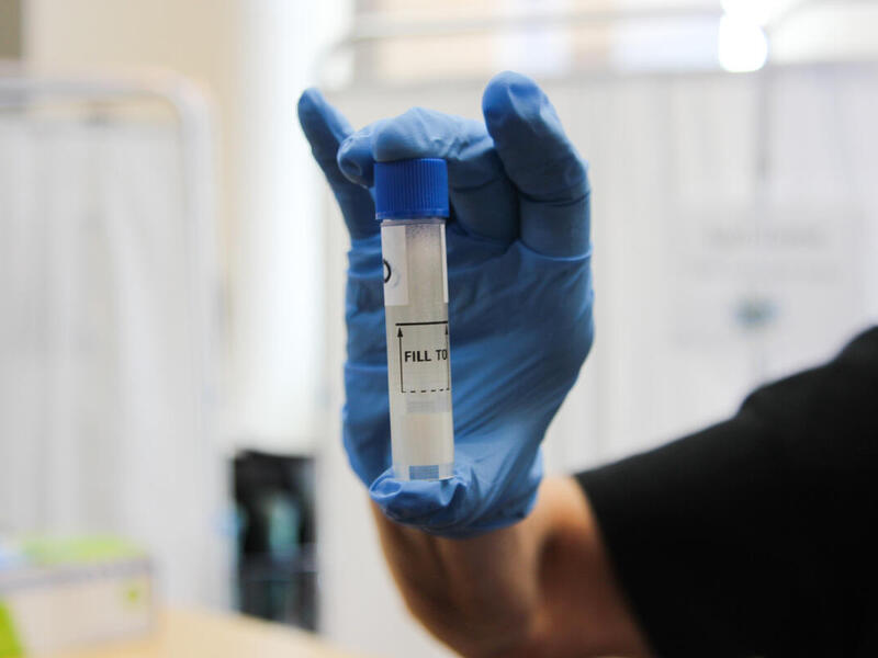 A photo of a hand wearing a blue latex glove holding a plastic beaker. 