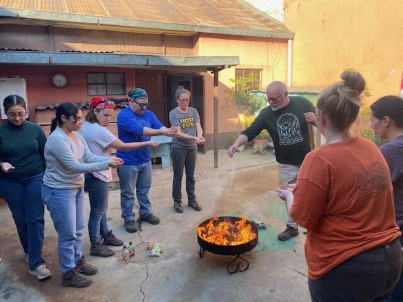 A photo of eight people standing around a fire 