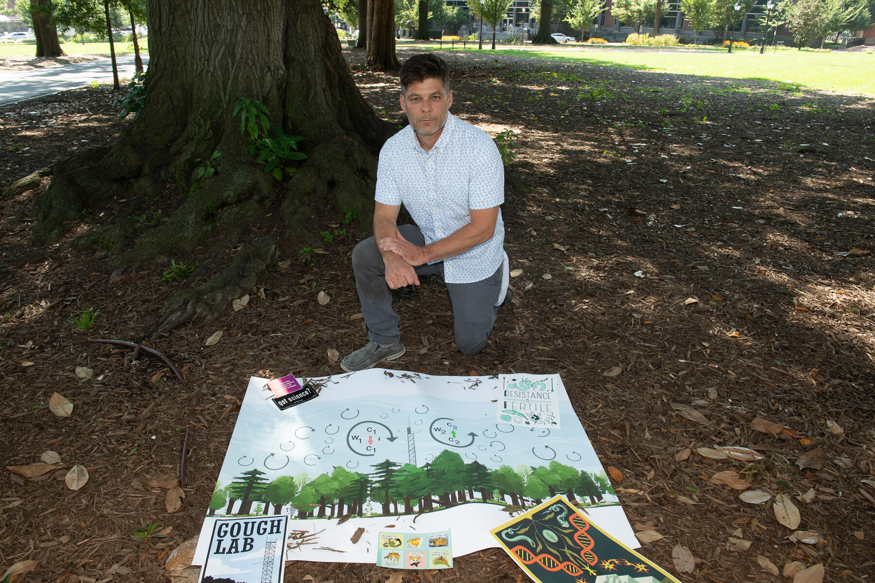 Biology professor Chris Gough, Ph.D., stands in Monroe Park while holding a piece of art produced by one of his students.
