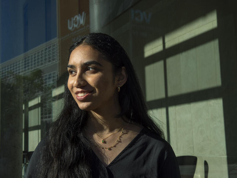 A photo of a woman from the best up looking to the left. She is wearing a black v-neck blouse and two gold necklaces. 