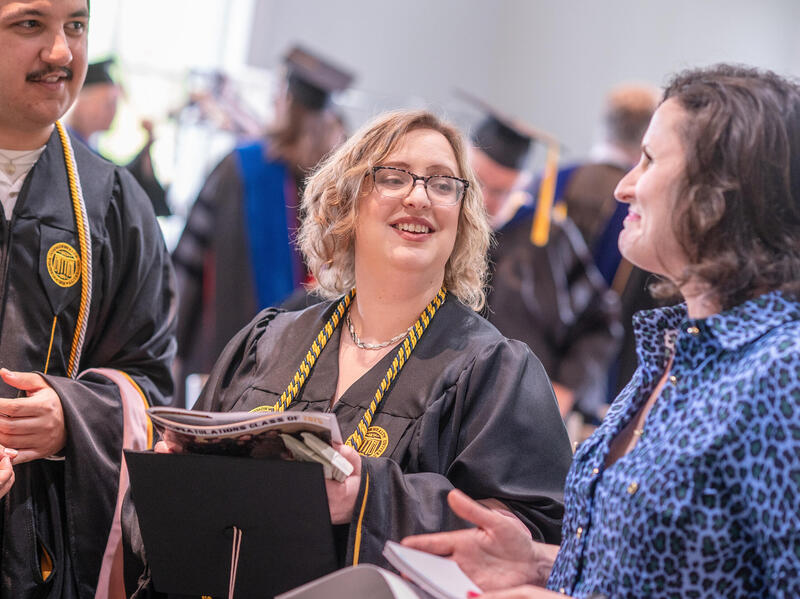 A photo of three people. The two people on the left are wearing college graduation gowns. 
