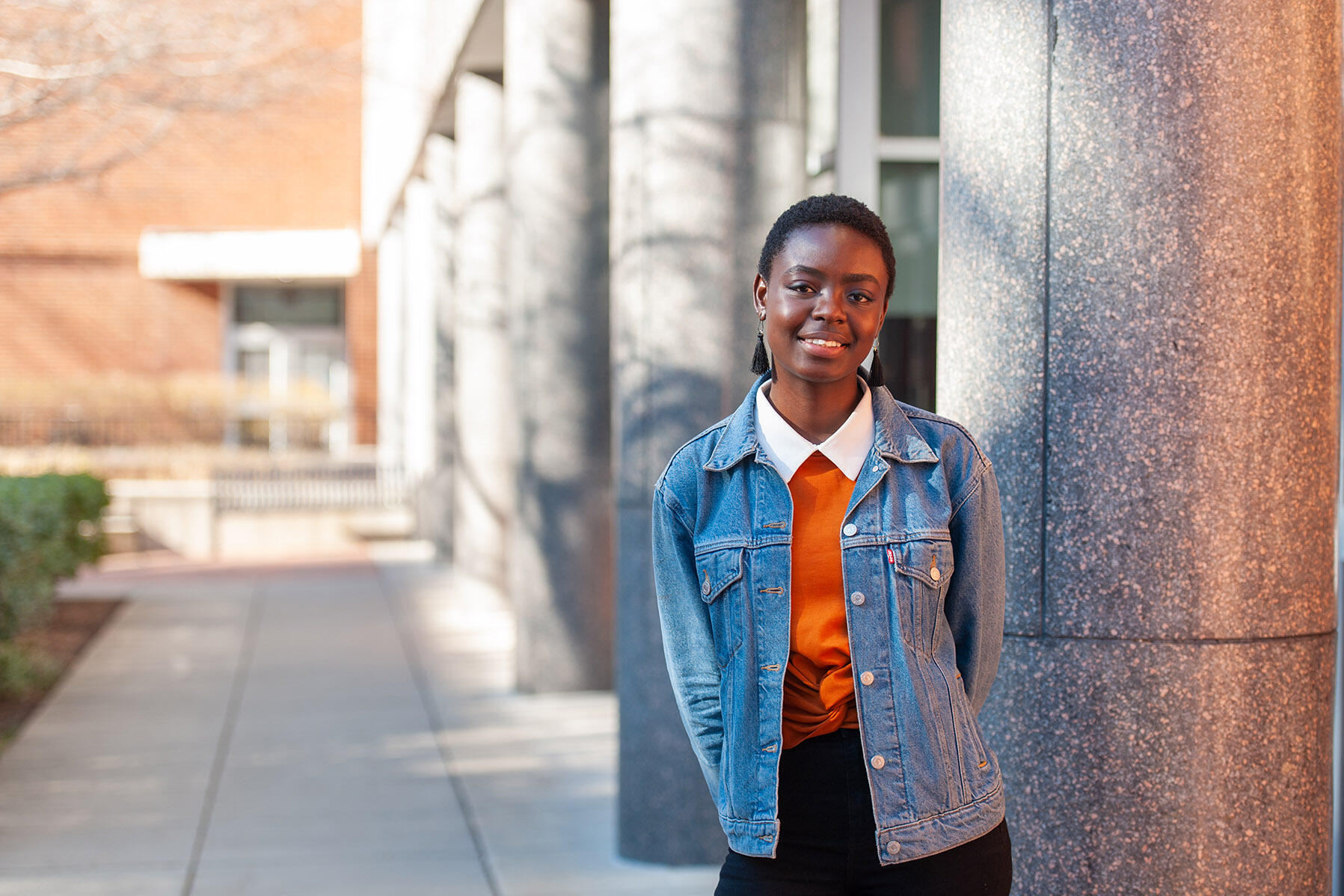 Woman in jean jacket standing next to column.