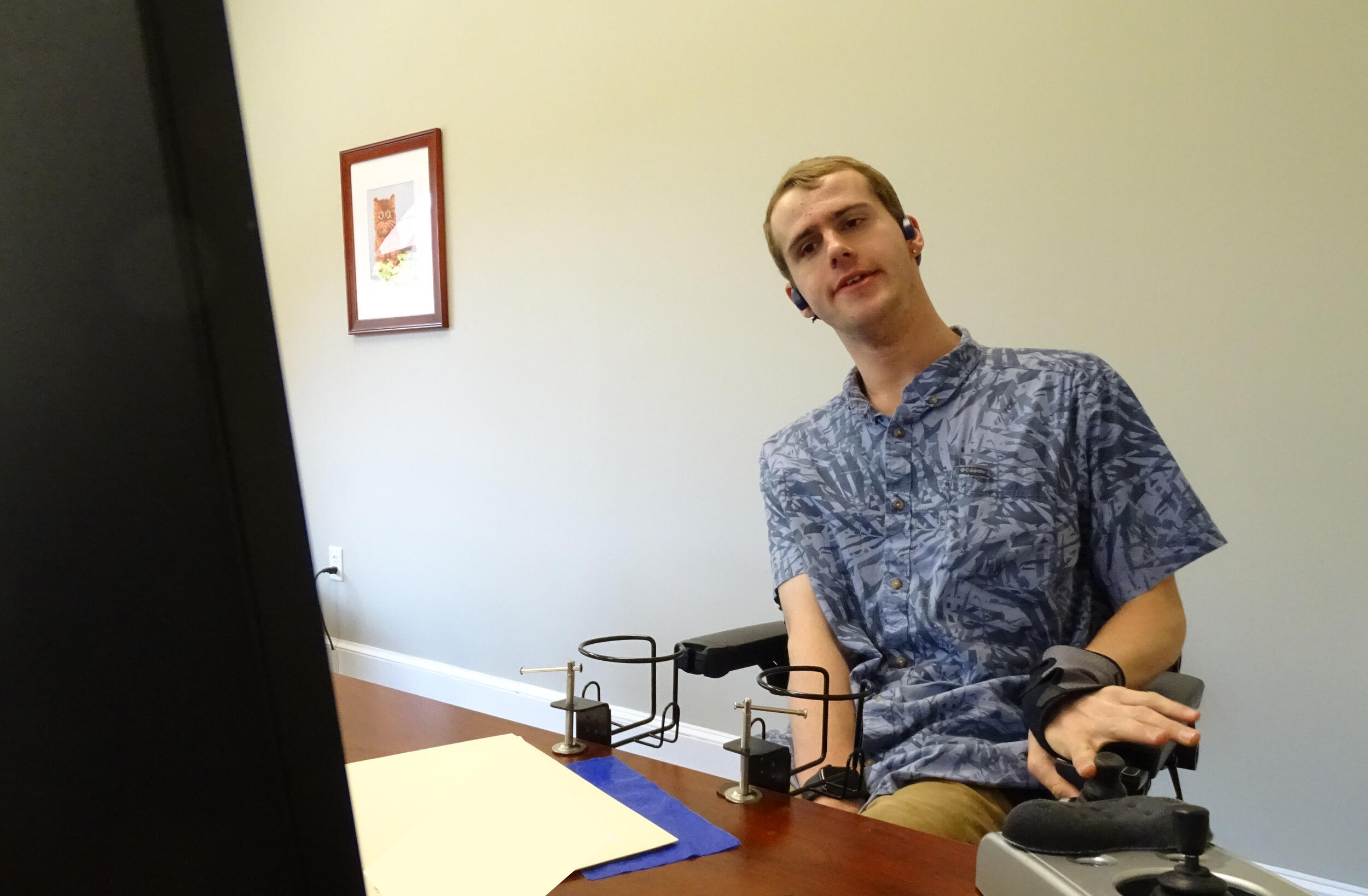 A man sits in front of a computer screen and uses an assistive technology device.