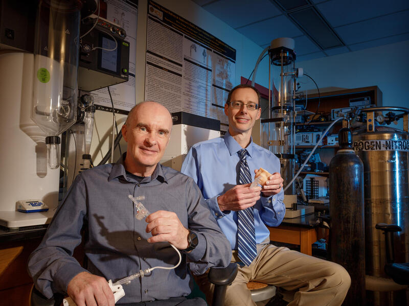 A photo of two men sitting in a lab. 