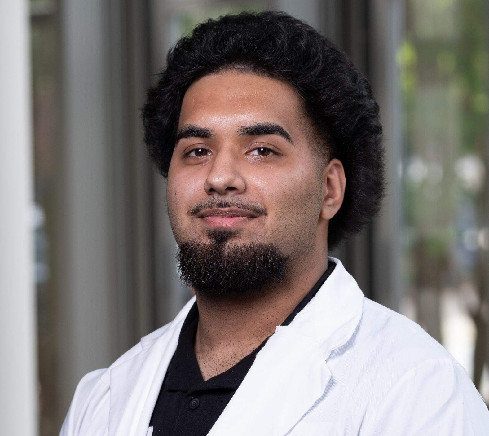 A photo of a man wearing a white lab coat from the shoulders up. 