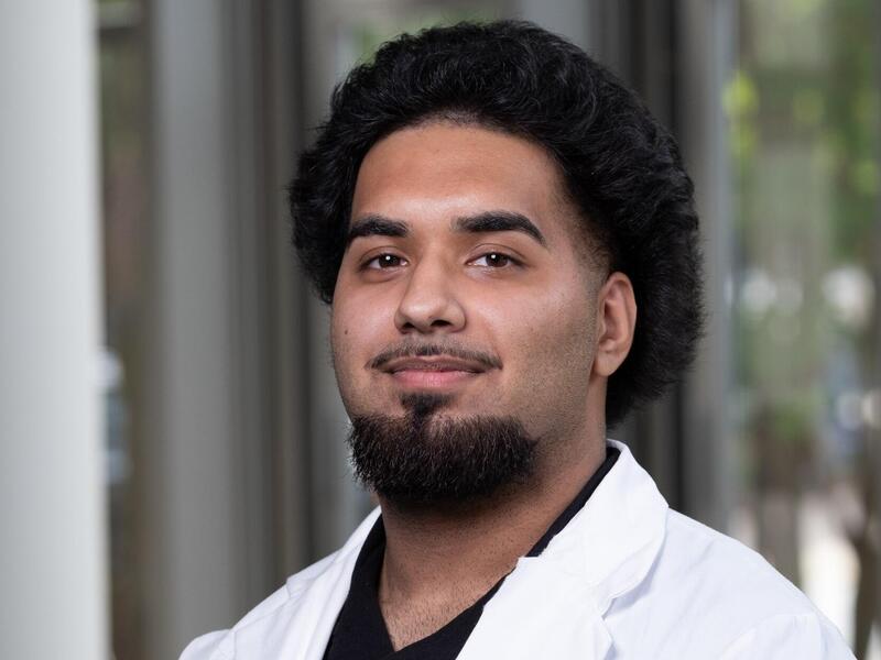 A photo of a man wearing a white lab coat from the shoulders up. 