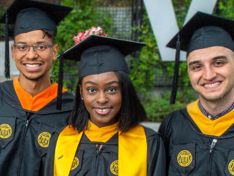 A group of three people in graduation attire, all smiling.