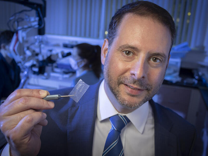 A man holding a small object in a research lab 