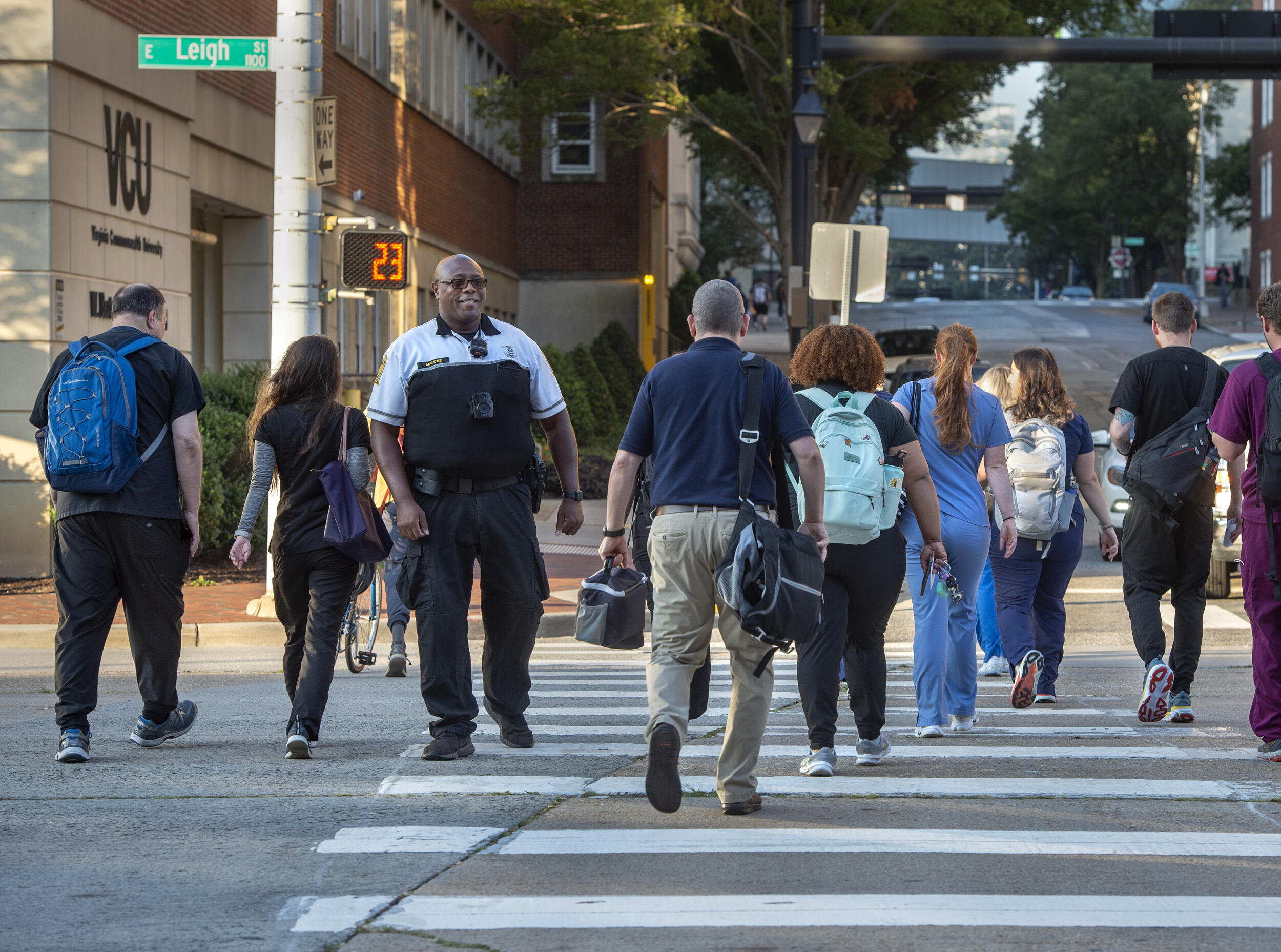 A smiling police officer greets people crossing the street in a crosswalk.