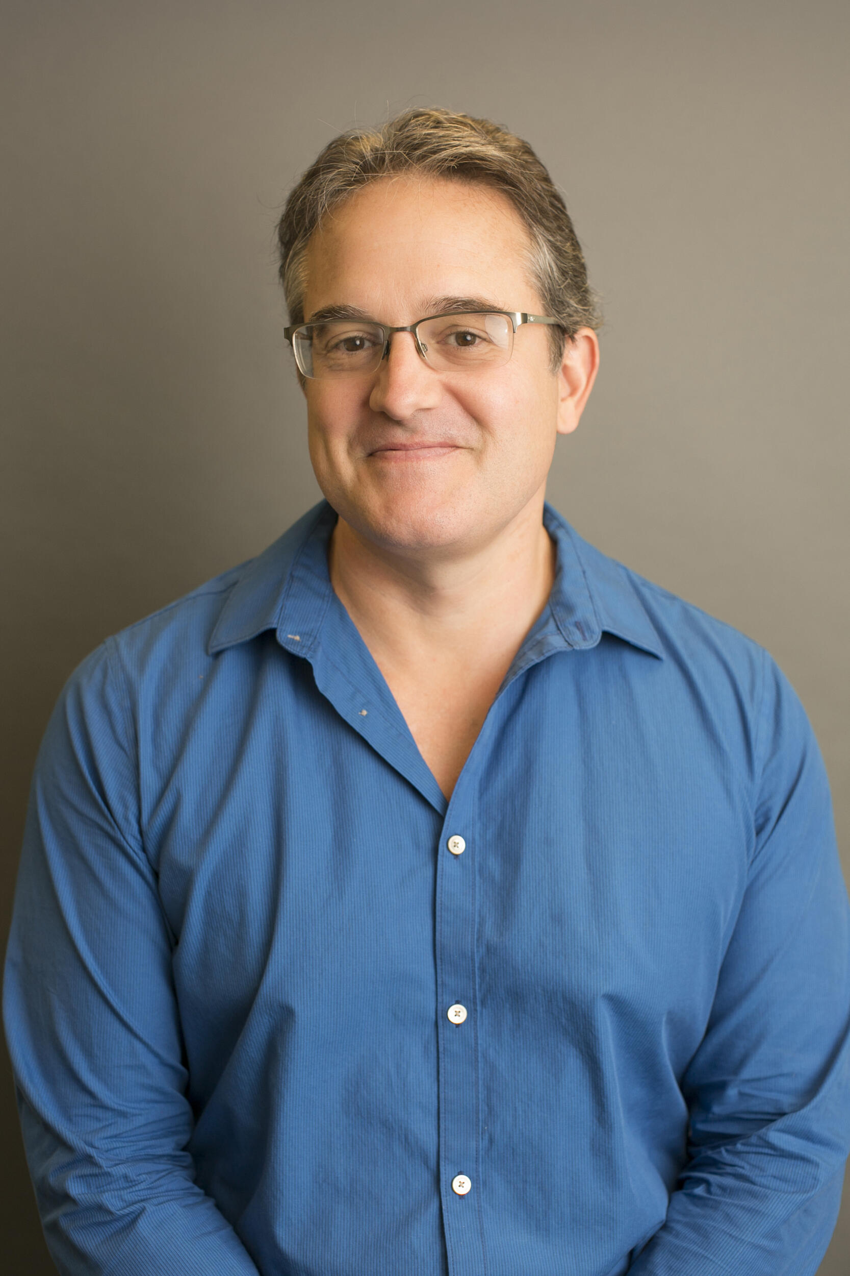 A photo of a man wearing a blue button down shirt and black glasses 