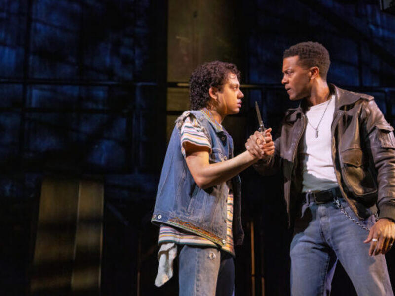 A photo of two men standing and facing each other staring at each other intensly. The men are also gripping each other's hand. 