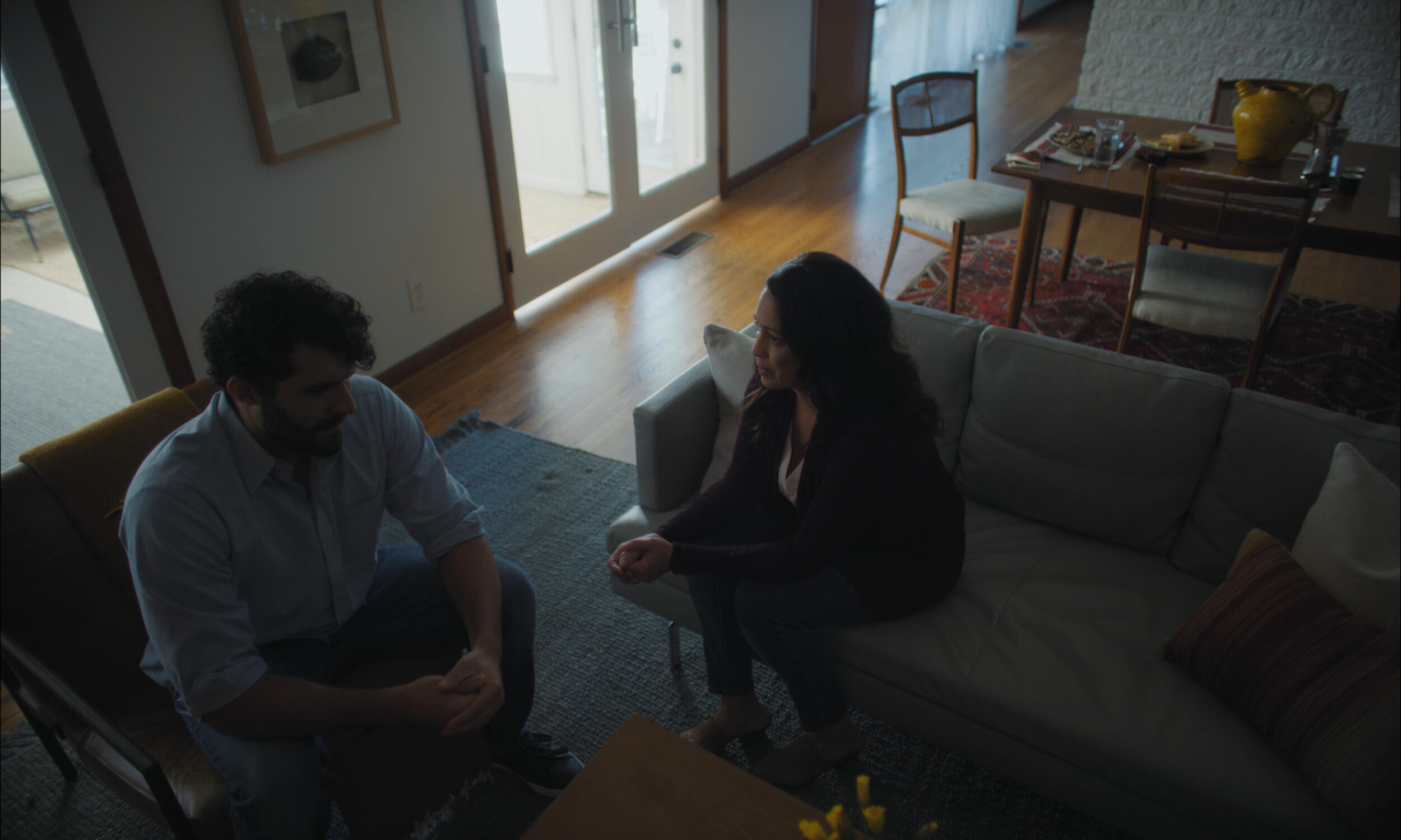 A man sitting to the left of a woman. The man is in a chair and the woman is sitting on a couch 
