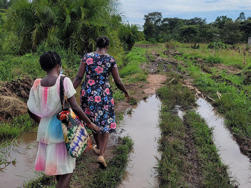 Two women walking on a dry patch of gras surrounded by large puddles. 