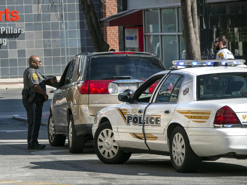 A police car parked behind an SUV. A police officer is standing next to the driver's window of the SUV.