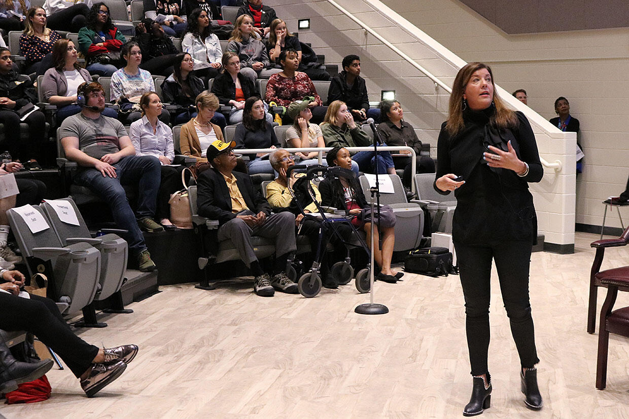 A person standing speaks in front of a crowd of people.