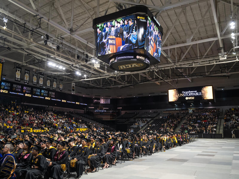 A photo of the Siegel Center full of people sitting the bleechers and graduates sitting on chairs on the court. 