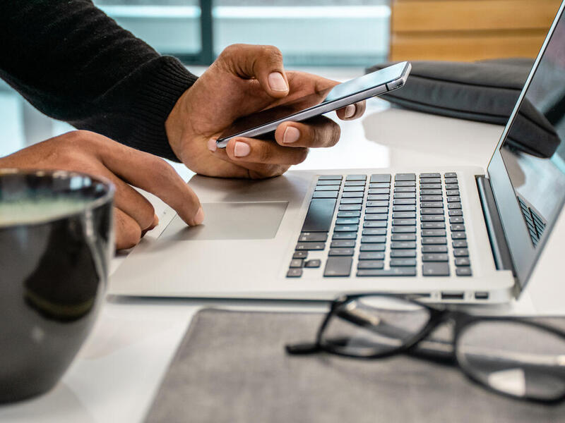 A person using a laptop computer and a cell phone.