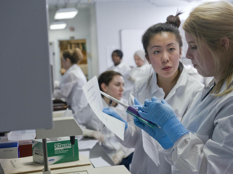 Women wearing lab coats and gloves in a research lab. 