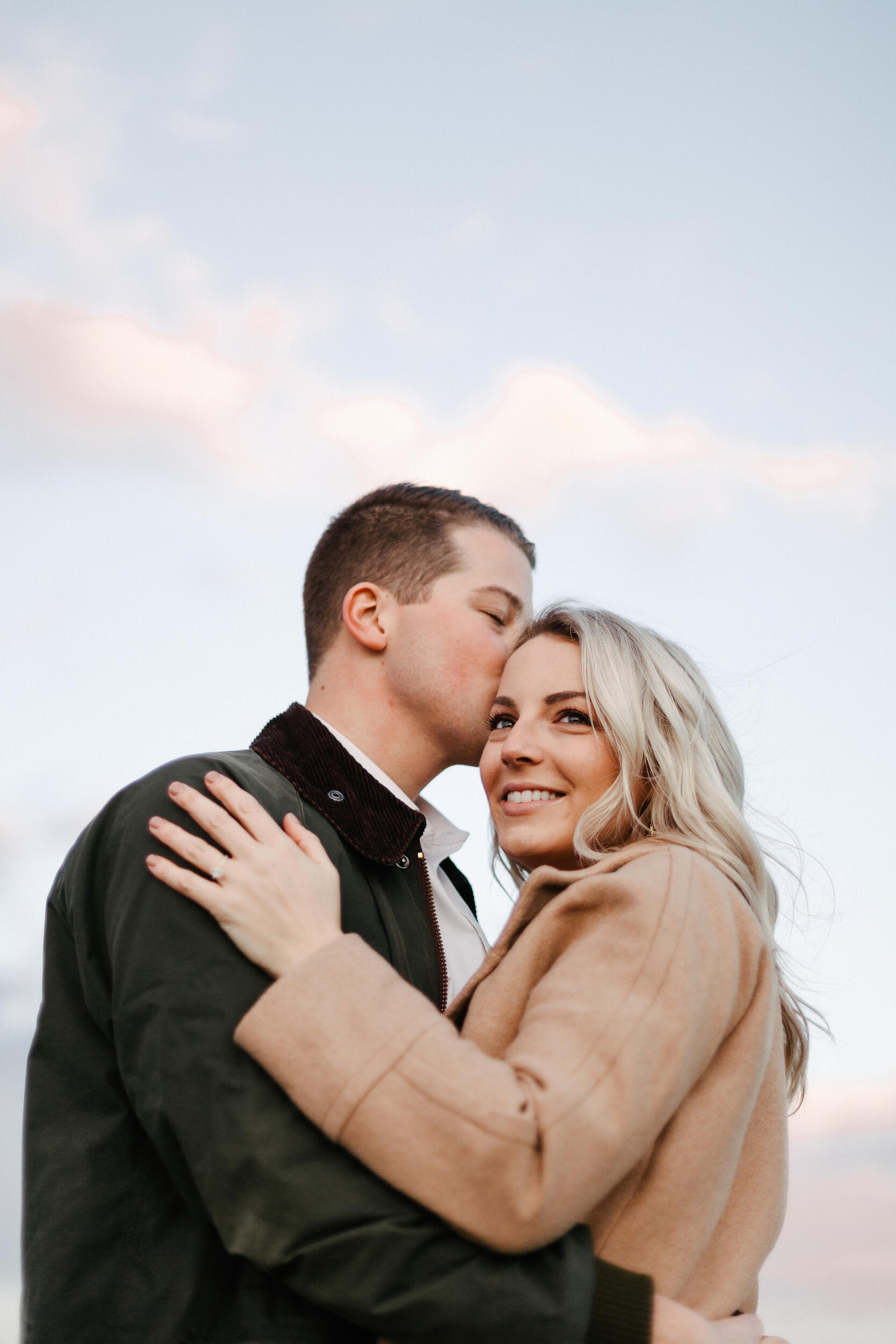 A man and woman holding each other with the man kissing the woman's head. 