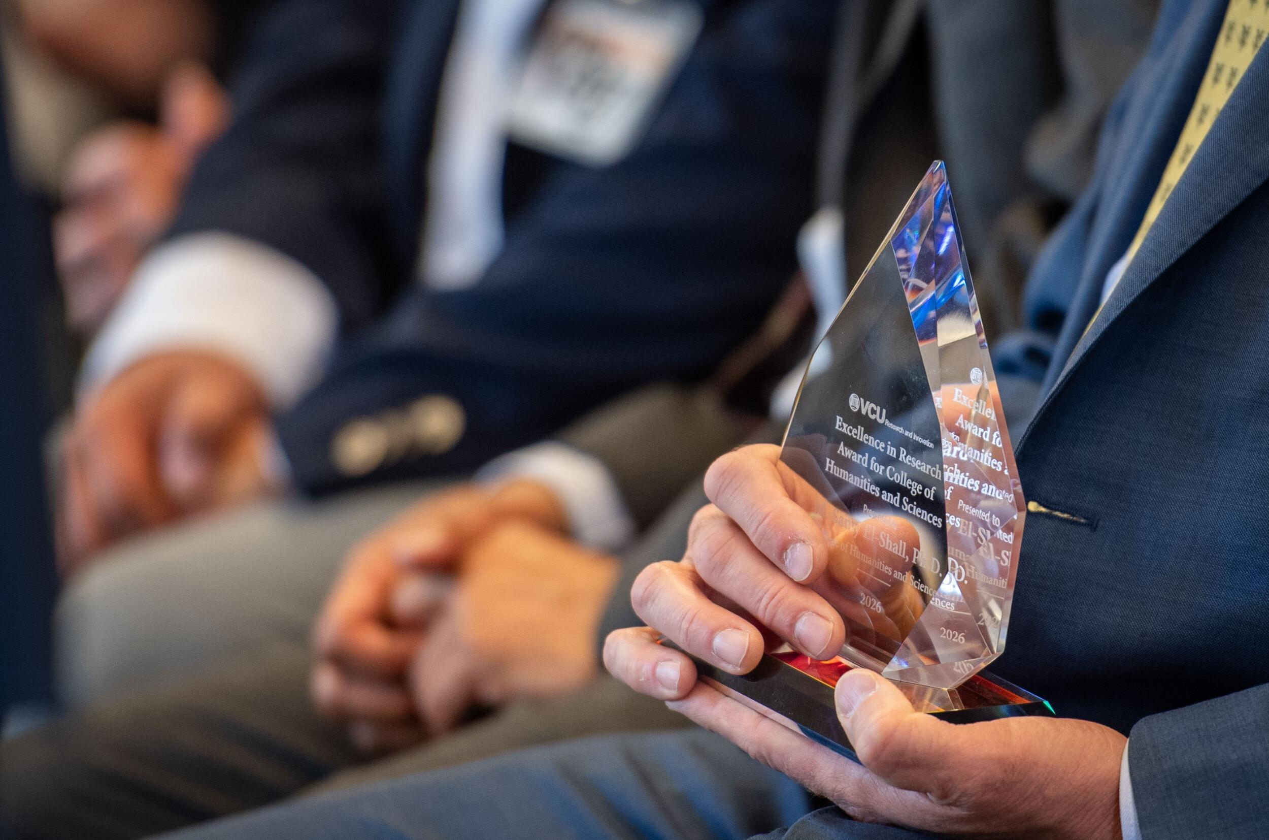 A photo of of a close up of a man's hands holding a glass award. 