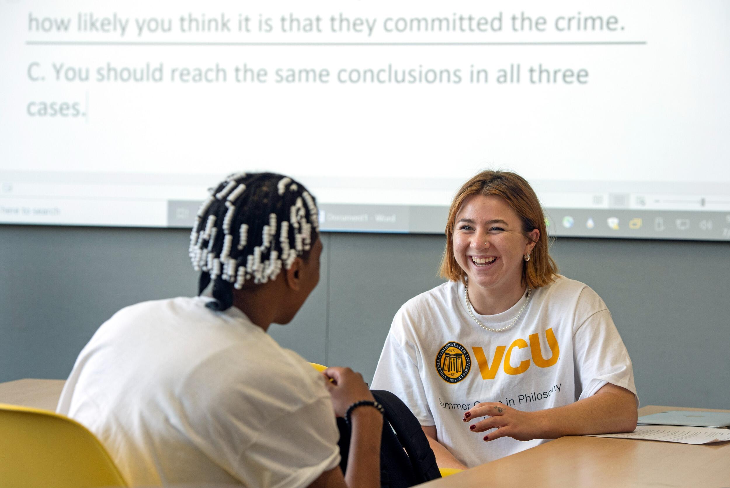 Katie Kerrigan and Amanda Nash face each other, sitting at a table, sharing a laugh.