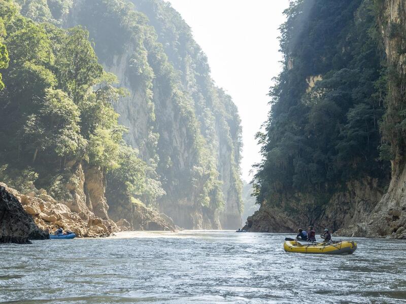 A photo of a boat going down a river between two cliffs 