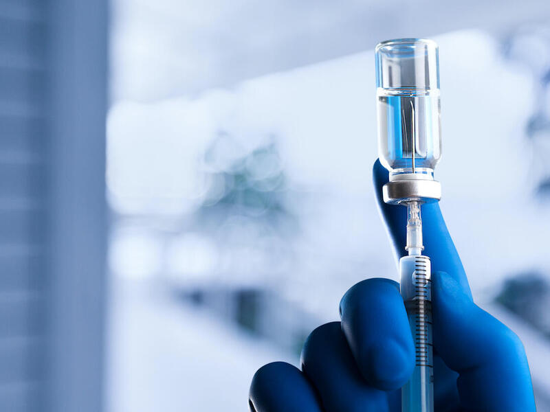 gloved hand fills a vaccine syringe