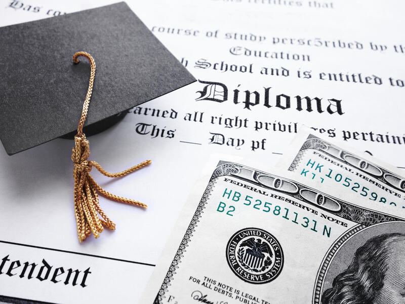 A photo of a diploma with a graduation cap and two hundred dollar bills on top of it. 