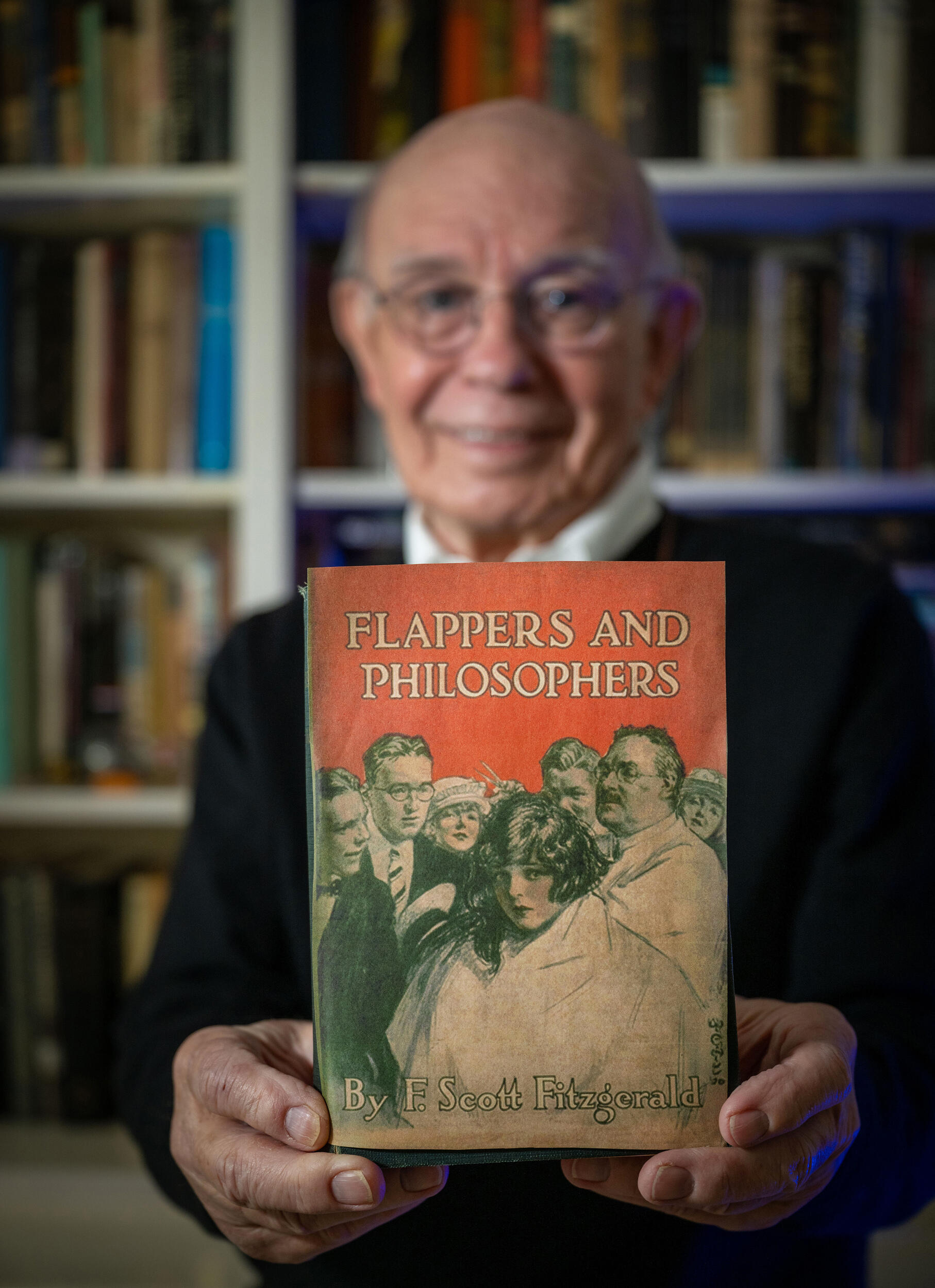 A photo of a man holding a book that says “Flappers and Philosophers, By F. Scott Fitzgerald”