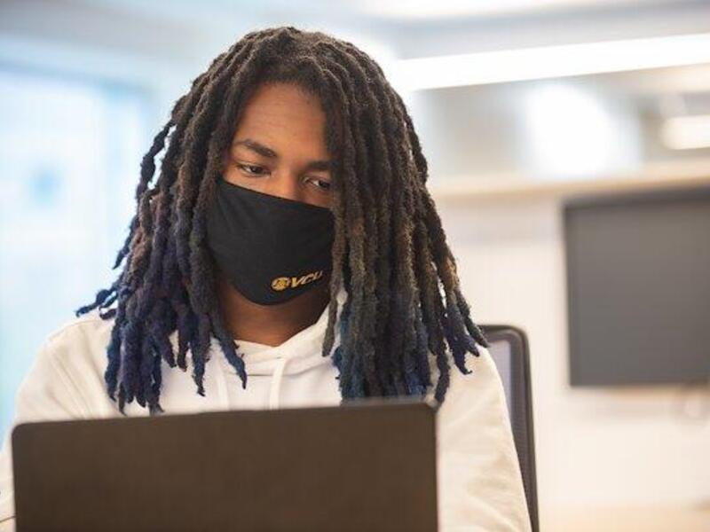 Photo of a student in a mask working on a laptop.