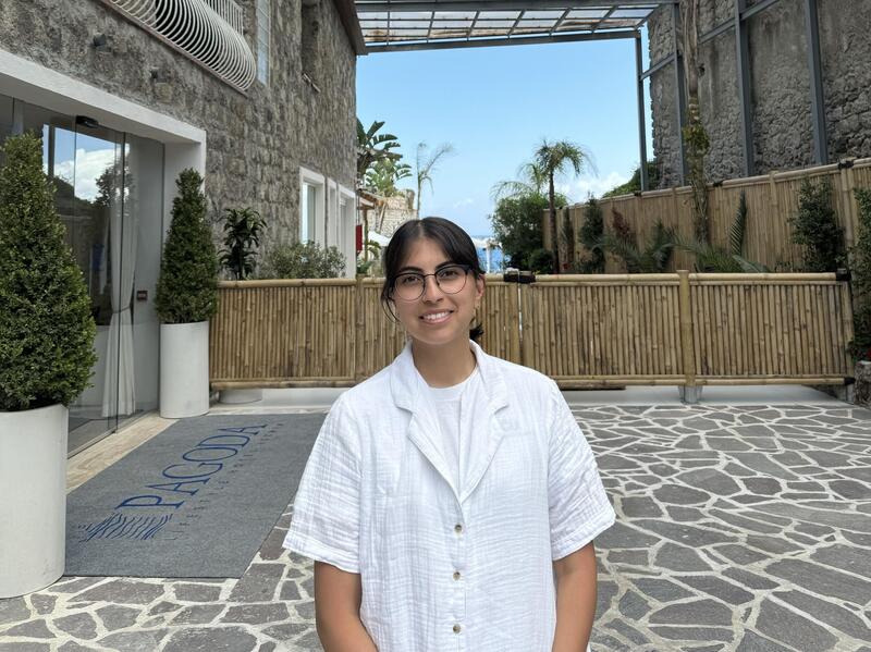 Woman in a white shirt standing near the entrance of a hotel.