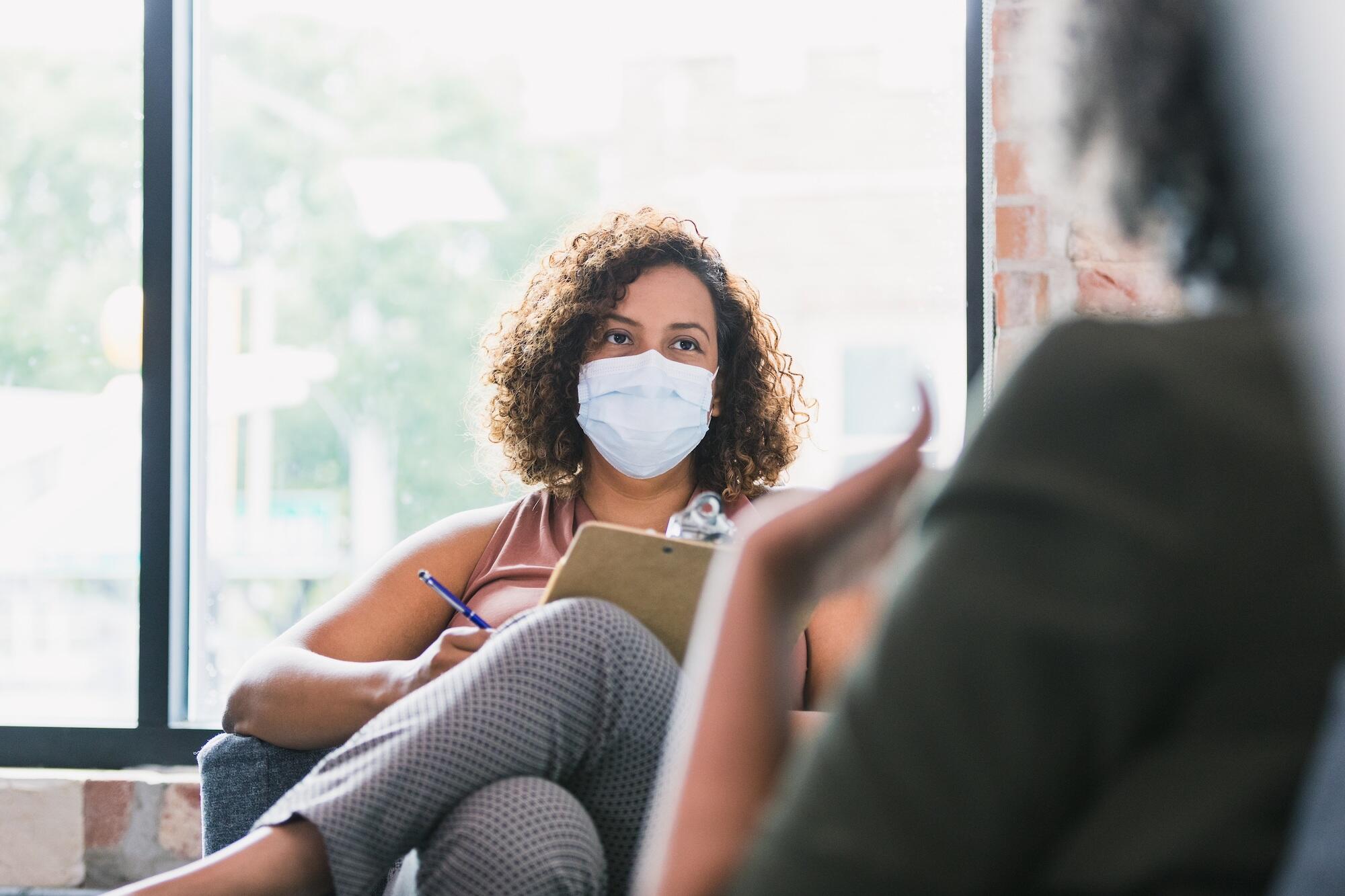 therapist wearing a mask and taking notes during a session with a patient