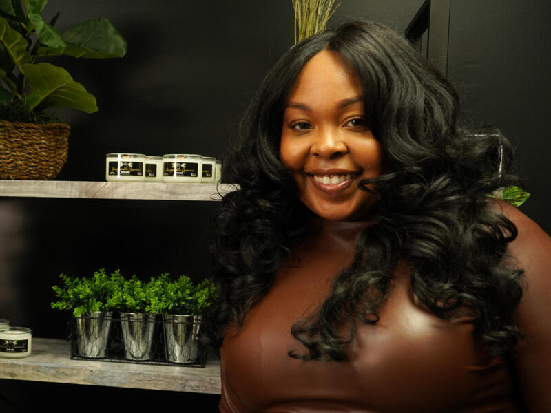 A woman with long curly black hair standing next to shelves that have plants on them. 