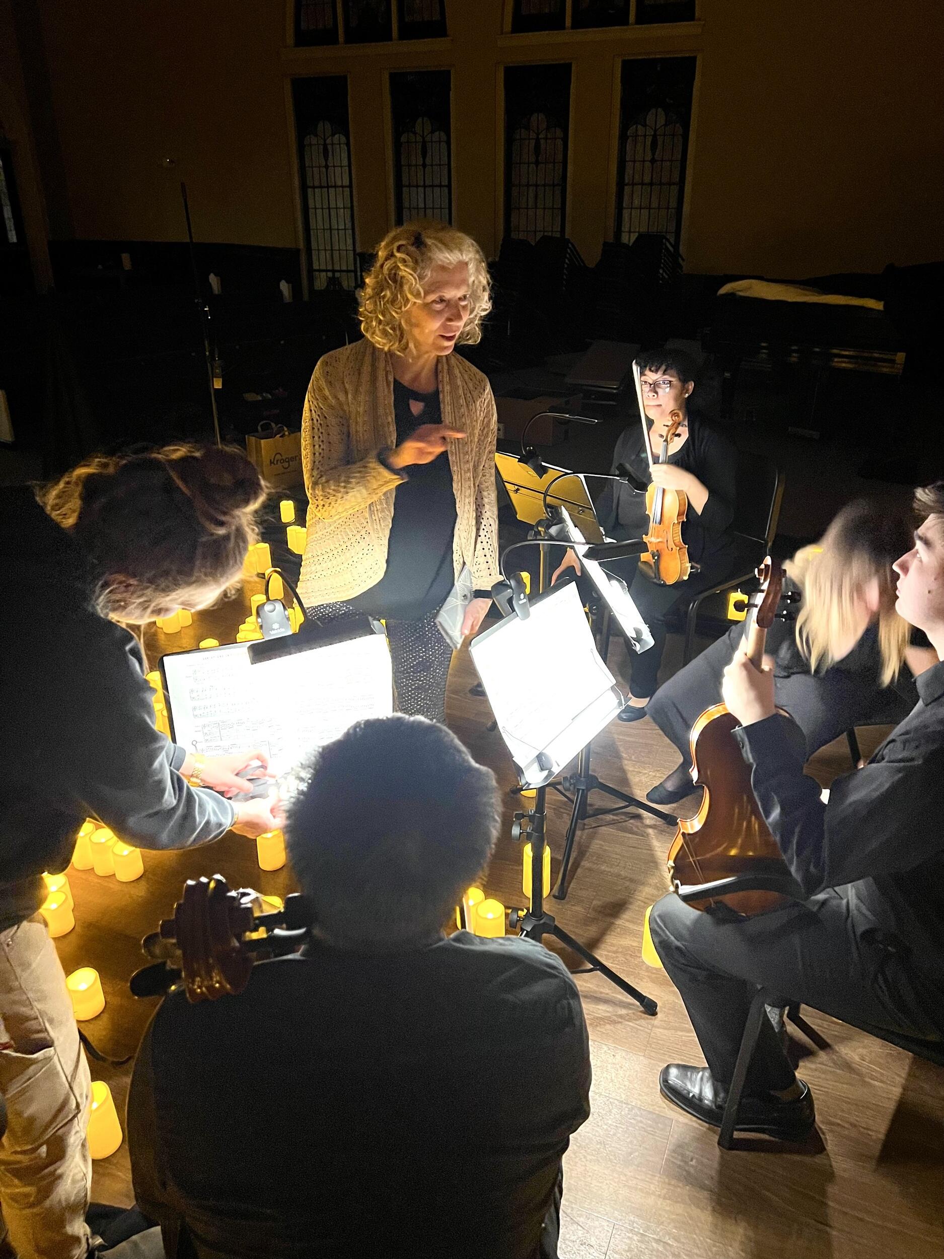 Professor Susanna Klein talks to student musicians on a candlelit stage.
