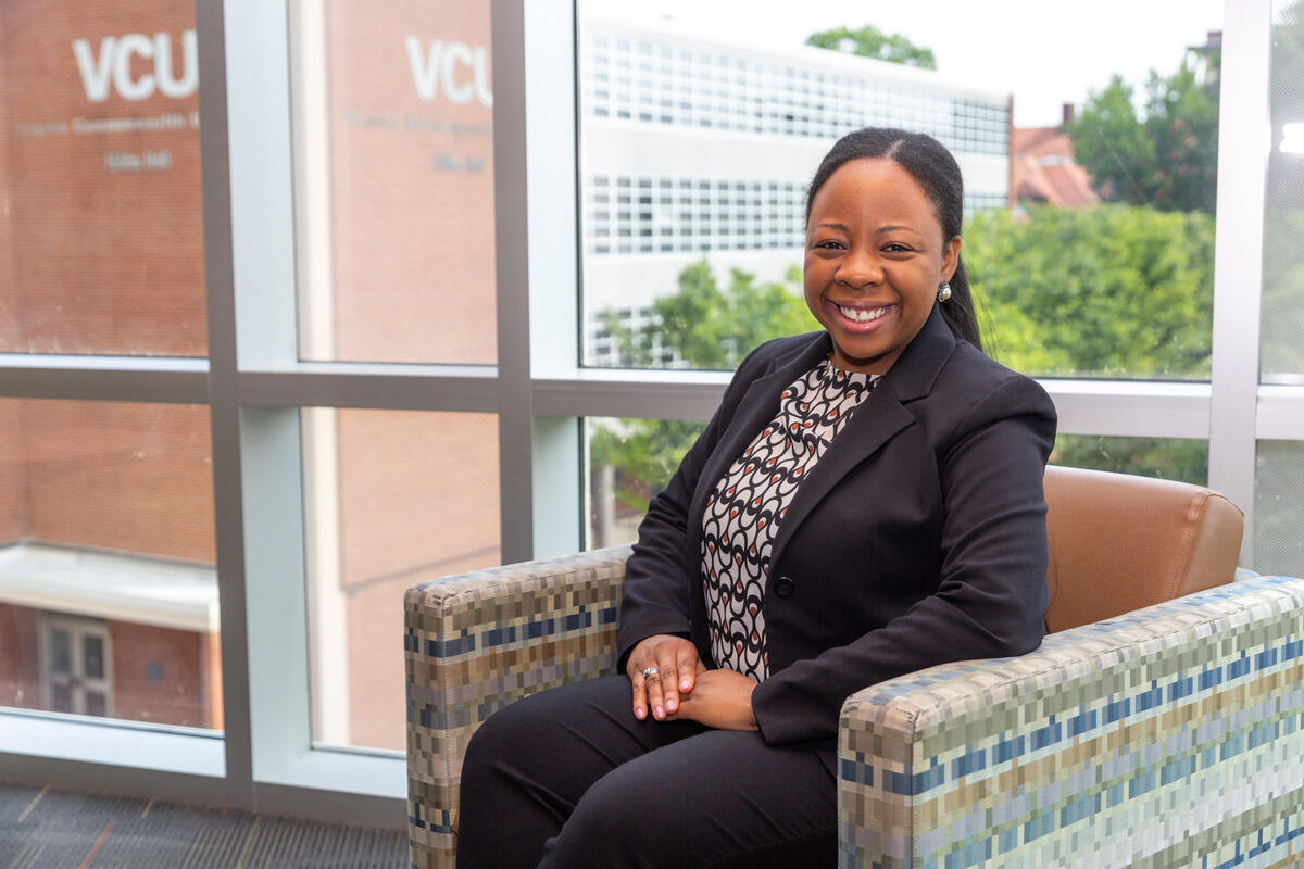 A woman smiling and sitting in a chair in front of a window. 