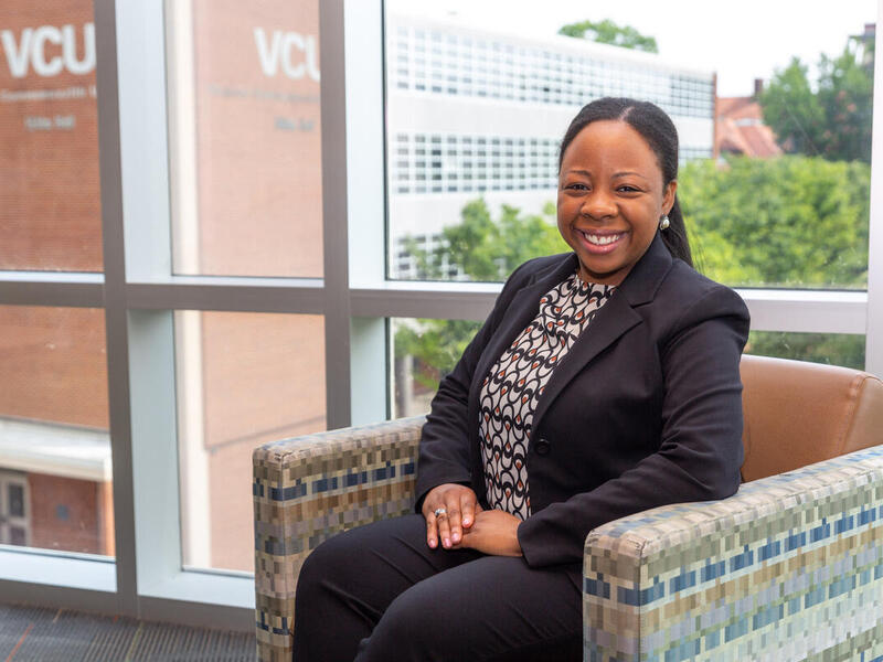 A woman smiling and sitting in a chair in front of a window. 