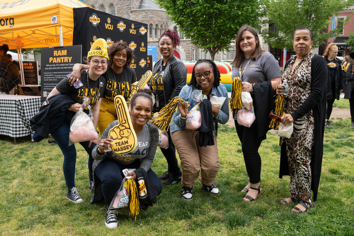 A group photo of seven people standing in grass. Next to them is a yellow tent 