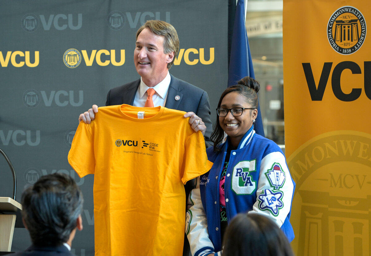 A photo of a man holding a tshirt while standing next to a teenage girl. 