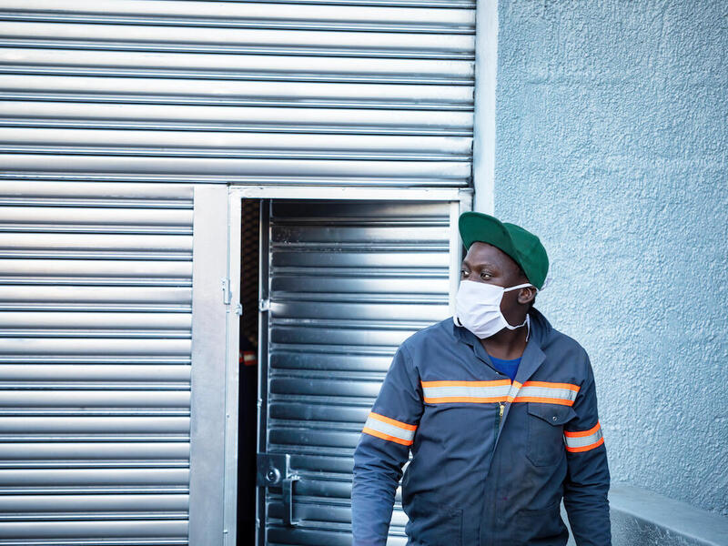 A person in a mask standing in front of a slightly opened door.