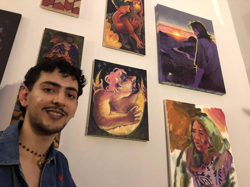 A person standing in front of paintings. 