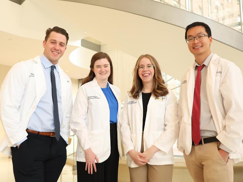 A group photo of four people standing in white coats. 