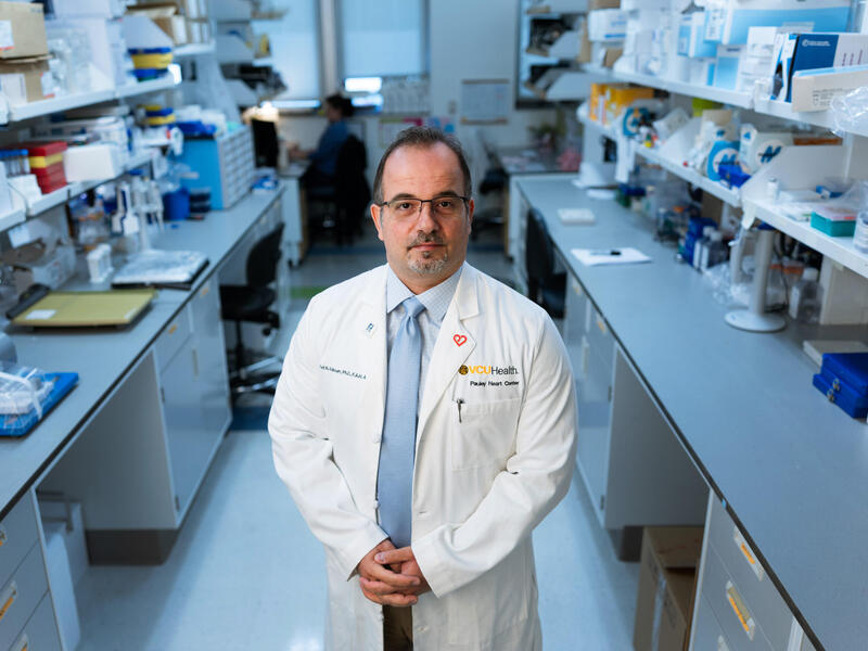 A man in a white lab coat stands in a lab environment.