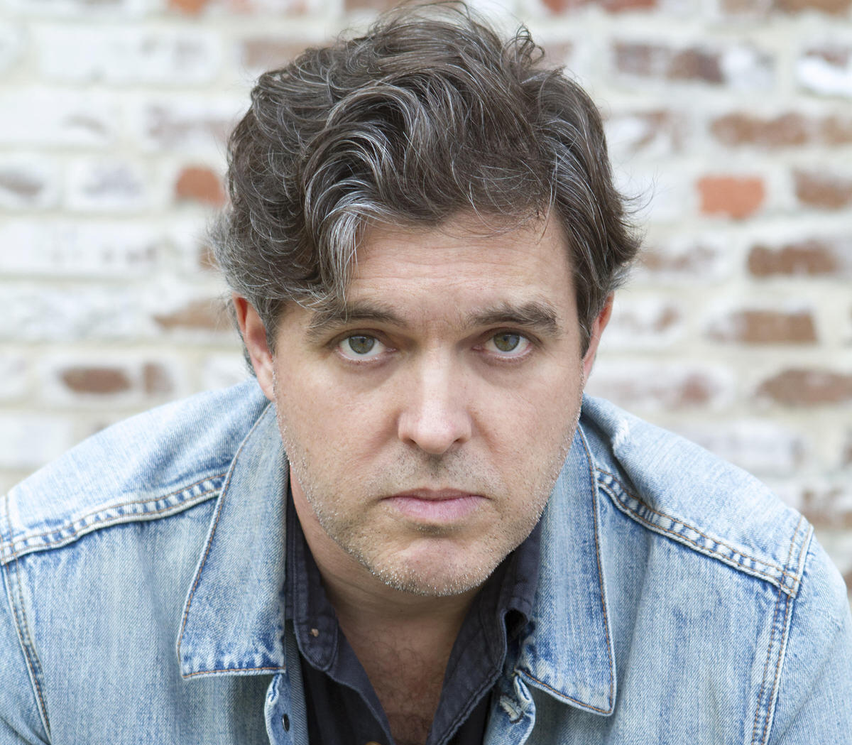 A photo of a man sitting in front of a brick wall 