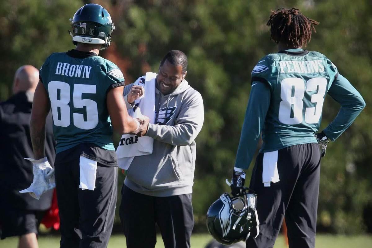 A man standing and smiling while holding a football players wrist. 