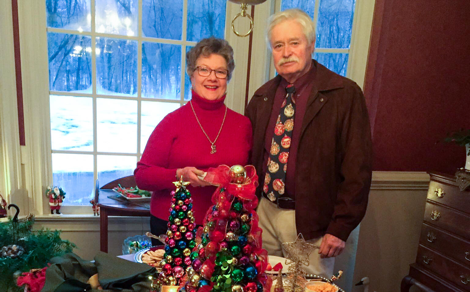 Two people stand behind a table with holiday decorations.